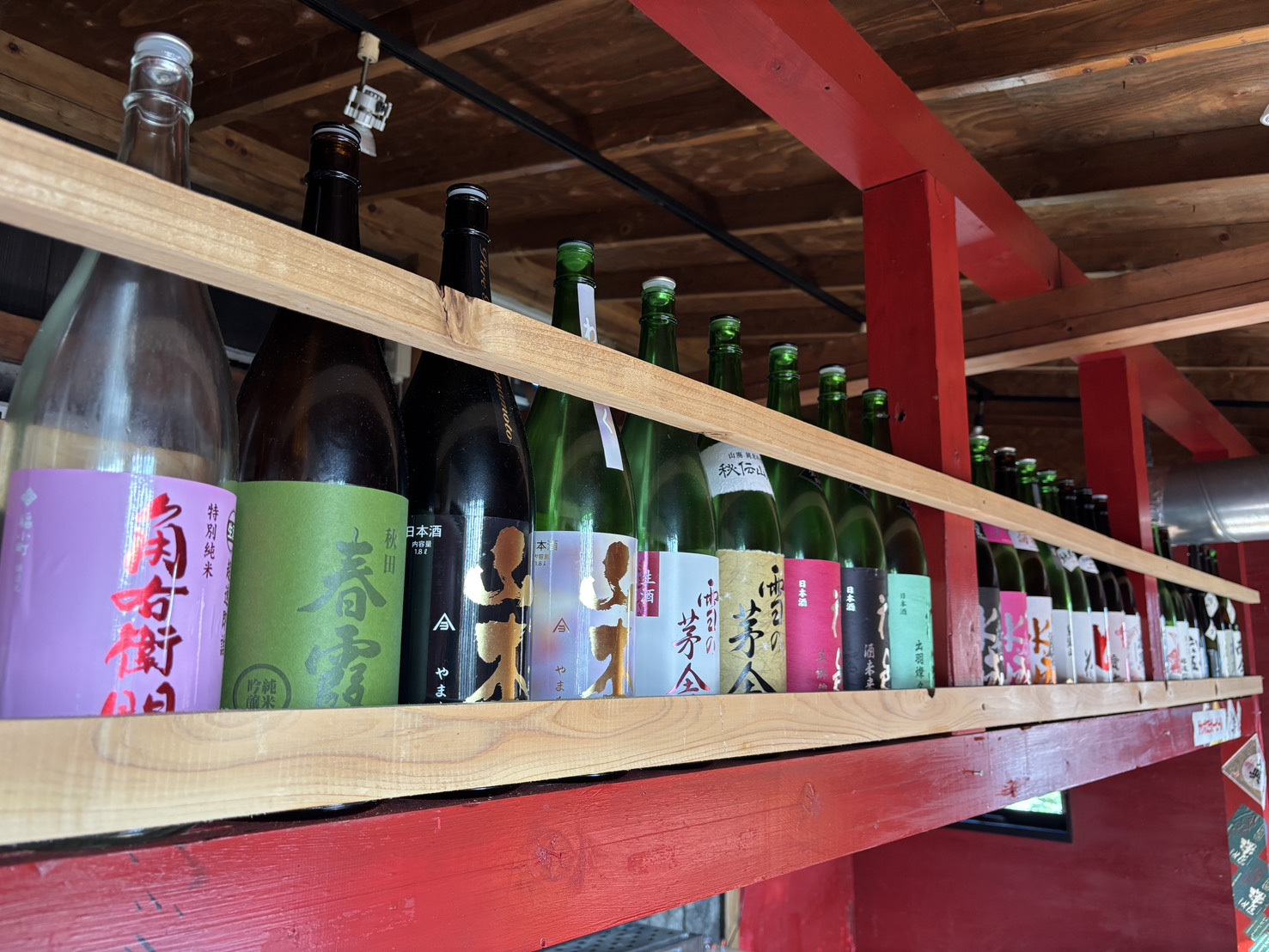 赤い梁の棚に並ぶ日本酒の瓶の列